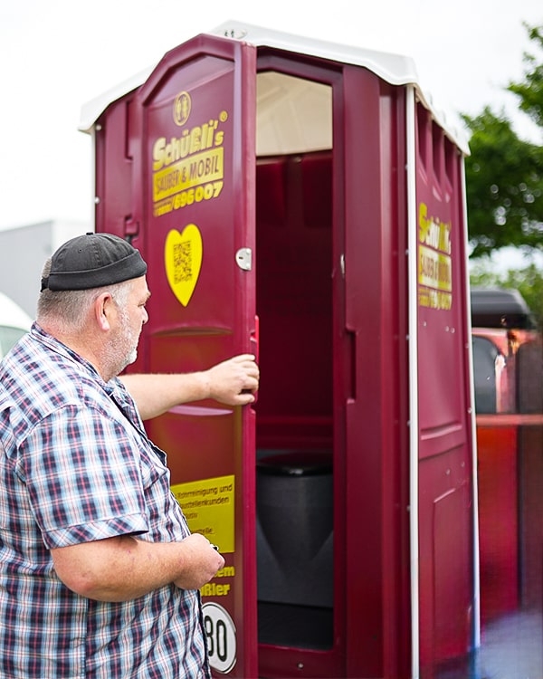Ein Kunde von Schüßler's Rohrreinigung öffnet die Tür von einer mobilen Toilette.